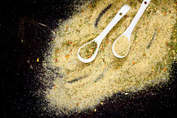 Salt with spices on a spoon, black background, top view.