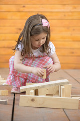 Portrait of beautiful little girl playing outside with wooden blocks, being inventive building a house for her toys