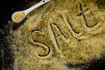 Salt with spices on a spoon, black background, top view.