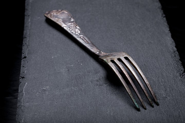 Fork on a plate of slate on a black background. Selective focus