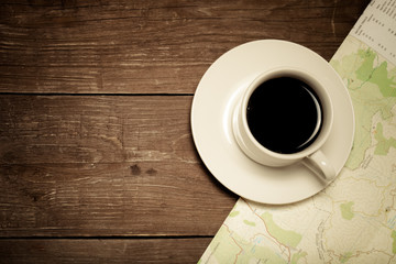 White cup of coffee and map on old wooden table. Toned