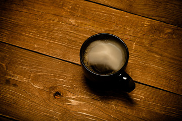 Black cup of coffee on old wooden table. Toned