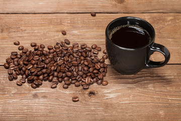 Black cup of coffee and coffee seeds on old wooden table
