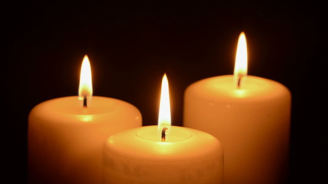 Three candles burning on a black background
