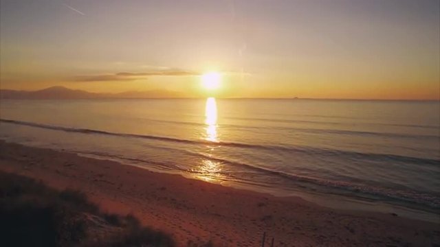 Idyllic drone footage of sea during sunset. Tilt up shot of fit woman standing on beach. Sporty female is with hands on hips. Scenic view of seascape and sun.