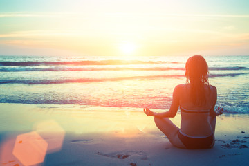 Young healthy woman practicing yoga on the beach at amazing sunset.