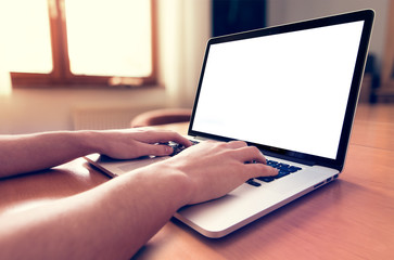 Man's hands using laptop with blank screen on desk in home interior.