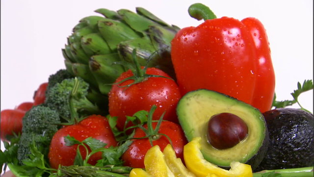 Zoom out shot of an assortment of vegetables rotating on a white screen.