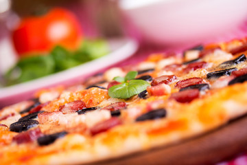 Homemade pizza with hunter sausages, bacon, olives and basil