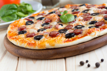 Homemade pizza with hunter sausages, bacon, olives and basil