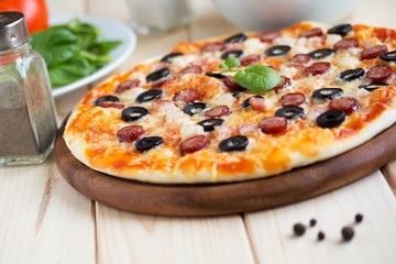 Homemade pizza with hunter sausages, bacon, olives and basil