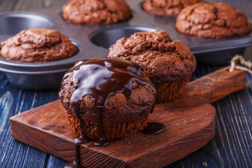 Chocolate muffins with chocolate syrup on dark background.
