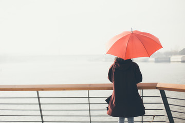 Woman standing at the balcony looking at the river and holding umbrella - obrazy, fototapety, plakaty