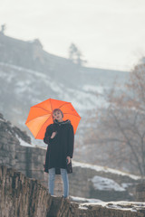 Young woman standing at the hill holding umbrella
