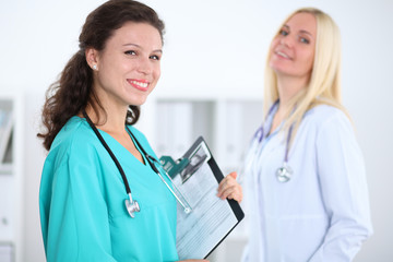 Fototapeta premium Two confident friendly female doctors sitting at the table and listen to the patient's history . Medical and health care concept
