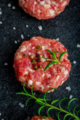 Raw burgers of beef and pork on a black board