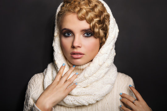 portrait of a beautiful young blonde woman on dark background. hair tied in a braid. girl wearing a warm sweater and scarf. copy space.