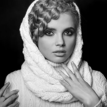 portrait of a beautiful young blonde woman on dark background. hair tied in a braid. girl wearing a warm sweater and scarf. copy space.