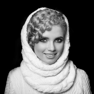 portrait of a beautiful young blonde woman on dark background. hair tied in a braid. girl wearing a warm sweater and scarf. copy space.
