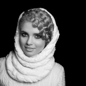 portrait of a beautiful young blonde woman on dark background. hair tied in a braid. girl wearing a warm sweater and scarf. copy space.