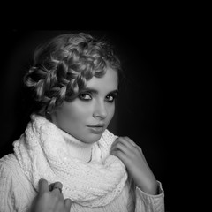 portrait of a beautiful young blonde woman on dark background. hair tied in a braid. girl wearing a warm sweater and scarf. copy space.