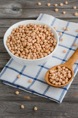 Raw dry chickpeas in a white bowl on the rustic wooden table.