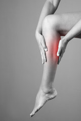 Pain in the calf muscle of the woman. Massage of female feet. Pain in the human body on a gray...