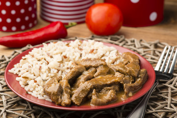 Stewed beef and rice on the red plate on brown wooden background.