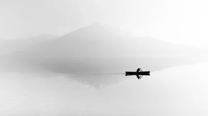Papier Peint photo Matin avec brouillard Fog over the lake. Silhouette of mountains in the background. The man floats in a boat with a paddle. Black and white