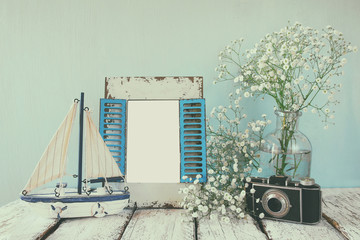 old vintage wooden frame, white flowers, photo camera and sailing boat on wooden table. vintage filtered image. nautical lifestyle concept. template, ready to put photography
