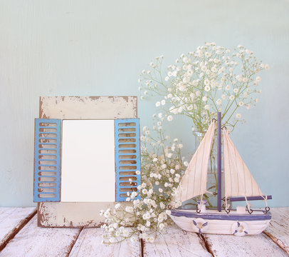 old vintage wooden frame, white flowers and sailing boat on wooden table. vintage filtered image. nautical lifestyle concept. template, ready to put photography
