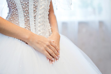 hands of the bride on background of wedding dress.