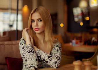 Portrait of a cute blonde smiling woman sitting in a cafe with a cap of coffee 