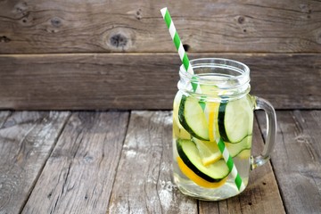 Lemon cucumber detox water in a mason jar glass with straw against a rustic wood background