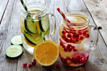 Detox water in mason jar glasses with lemon, cucumber and pomegranate against a rustic wood background