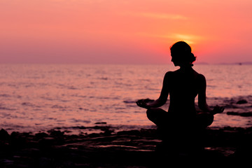 Woman silhouette sitting in lotus position on sunset sea background back lit