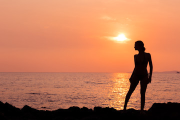 Standing woman silhouette on sunset sea background back lit
