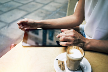 Cropped image with woman's hands touching screen of digital tablet at the table with cup of coffee