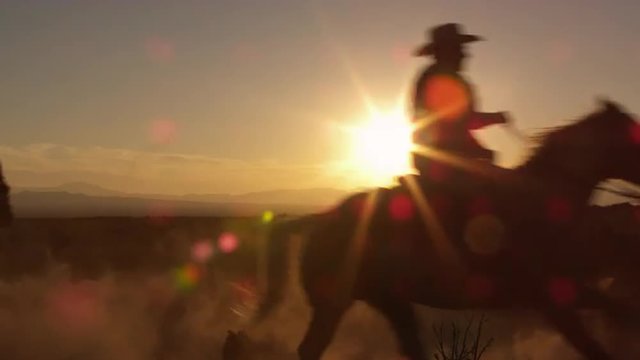 Cowboys galoping past the camera in slow motion during a golden sunrise sunset.