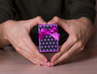 Two male hands in shape of heart holding purple spotted gift box