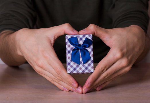 Two male hands in shape of heart holding checkered gift box with
