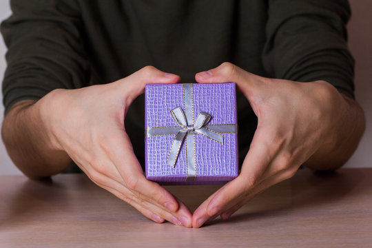 Two male hands in shape of heart holding lilac gift box