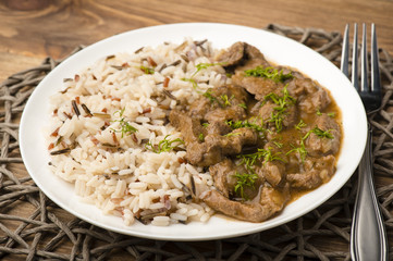 Stewed beef and rice on the white plate on wooden background.