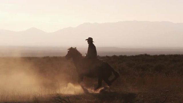 Slow motion silhouette shot of a cowboy riding a hourse in a circle