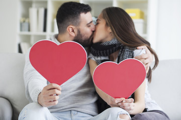 Two young dates kissing behind paper heart.Two young dates behind paper heart with their faces close to one another