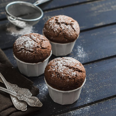 Delicious vegan chocolate muffins with icing sugar on dark wooden surface