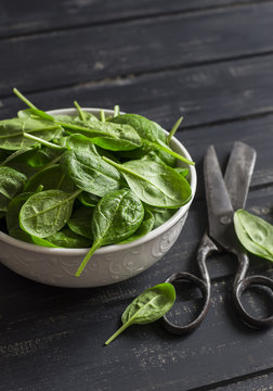 Fresh spinach in a white bowl on a dark wooden background. Healthy food