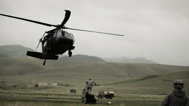 Shot from field of Black Hawk helicopter and soldiers preparing to haul off cargo.