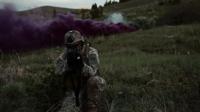 Soldier firing an automatic assault rifle in the direction of the camera while in a kneeling stance.