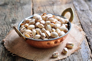 Pistachio in a copper bowl on the old wooden background